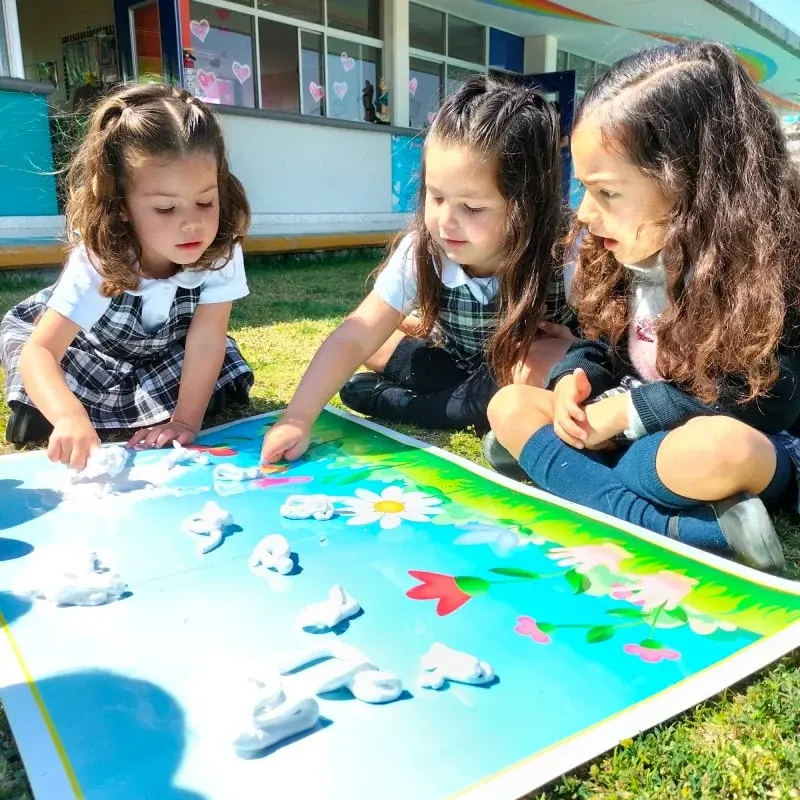 Tres alumnas del instituto trabajan juntas en una actividad artística colaborativa sobre el césped durante clase al aire libre.