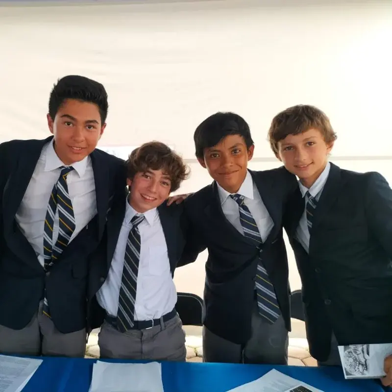 Cuatro estudiantes de uniforme escolar posando juntos en evento del colegio